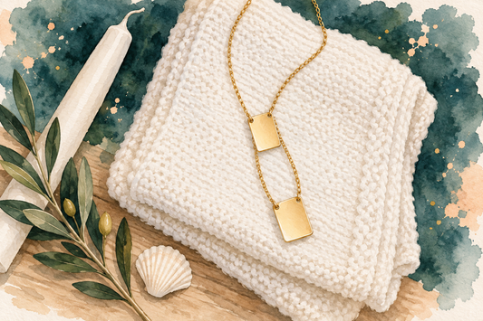 Ilustração em aquarela de um colar escapulário dourado de aço inox, com duas plaquinhas lisas, sobre uma manta branca de bebê, ao lado de uma vela de batismo, um ramo de oliveira e uma concha